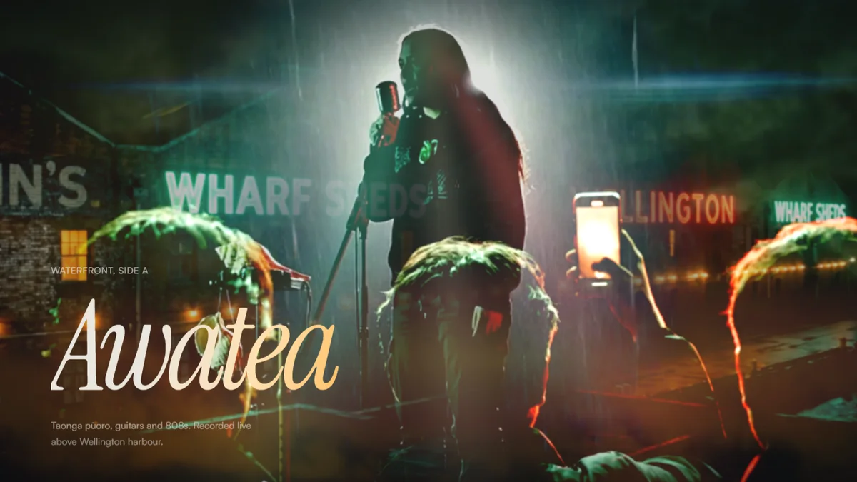 AWATEA music artist website, a singer rim-lit on a wet rooftop stage above Wellington harbour with the crowd in silhouette