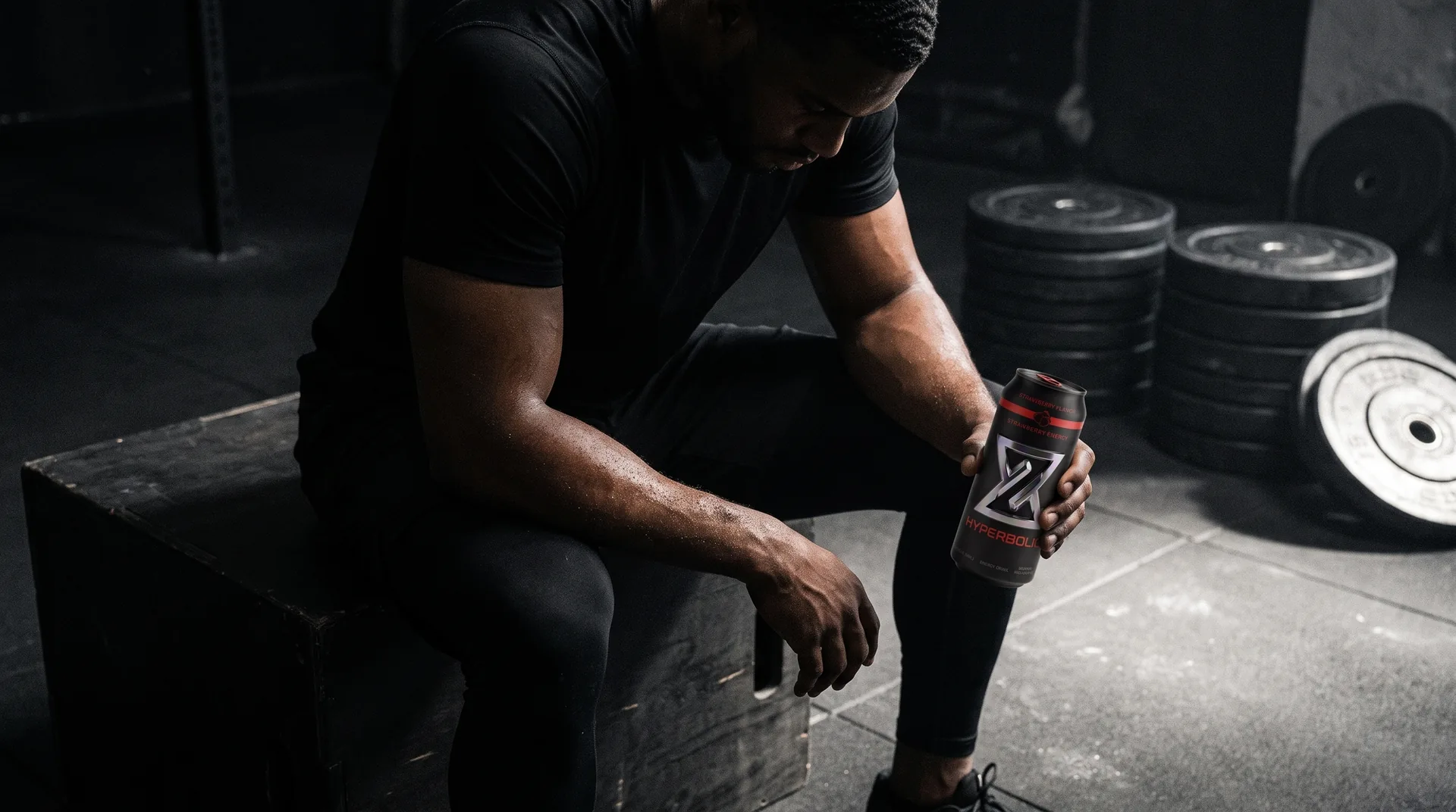 An athlete resting between sets on a plyo box, holding a HYPERBOLIC can